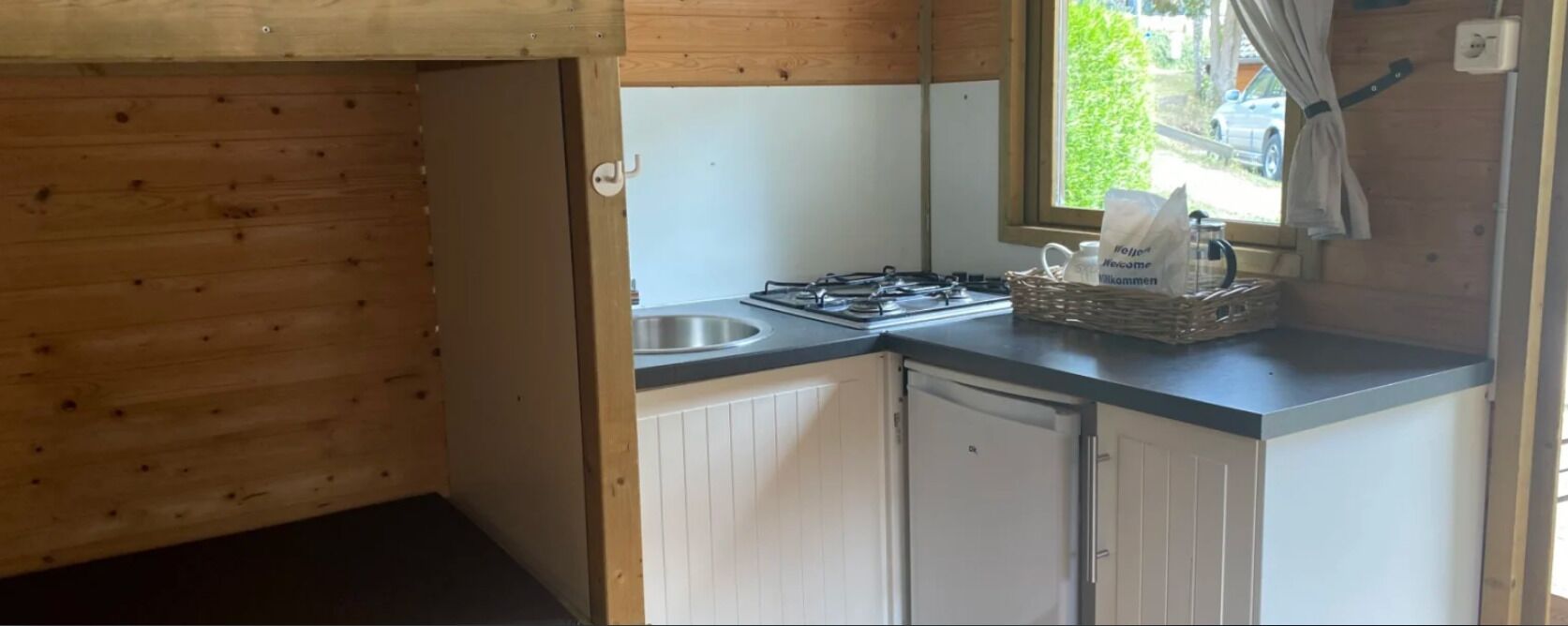 Une cuisine de taille réduite, équipée d’une cuisinière à gaz, d’un évier et de meubles blancs.