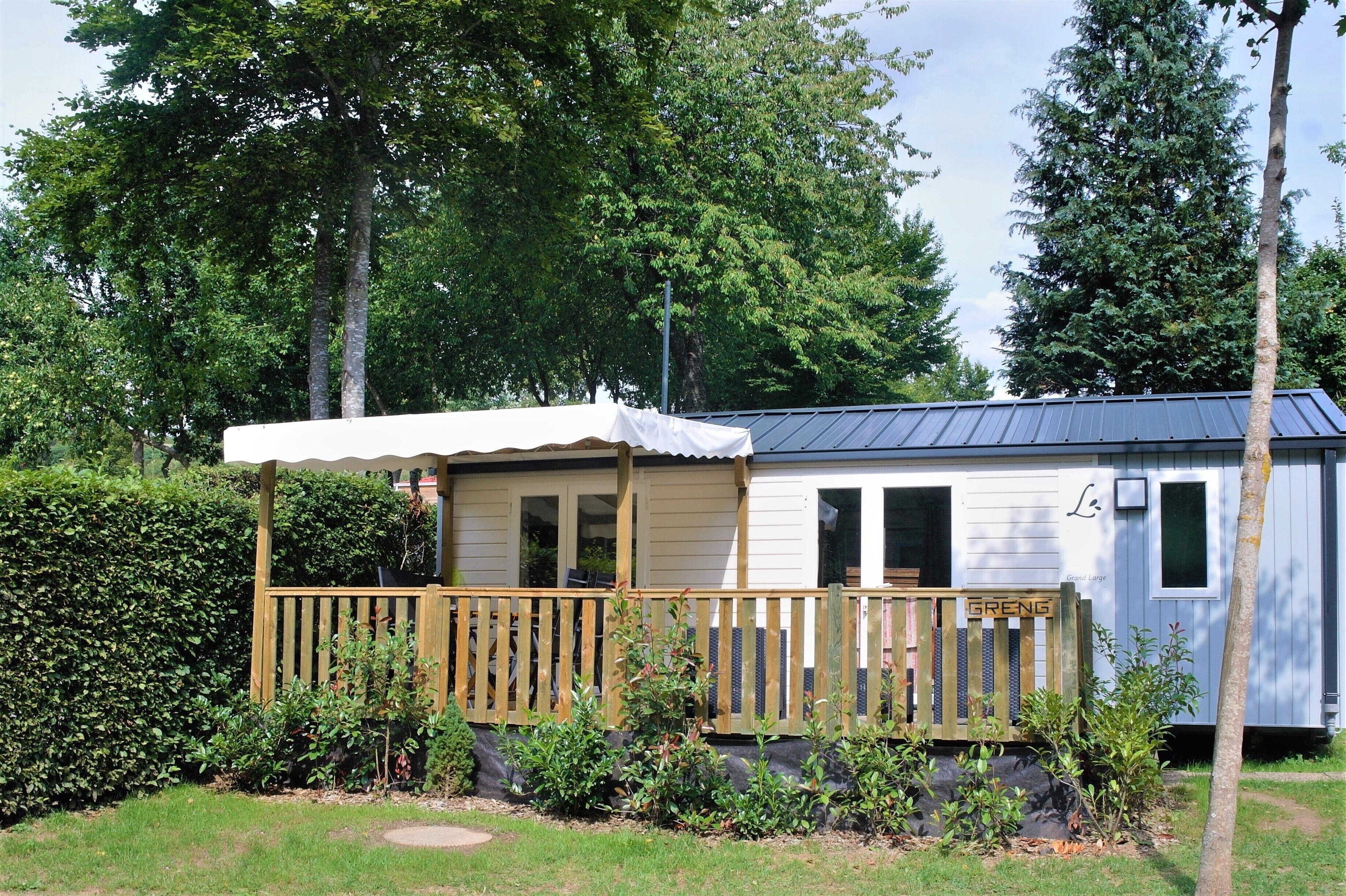 A mobile home with a wooden deck, a covered porch, and a small garden area.
