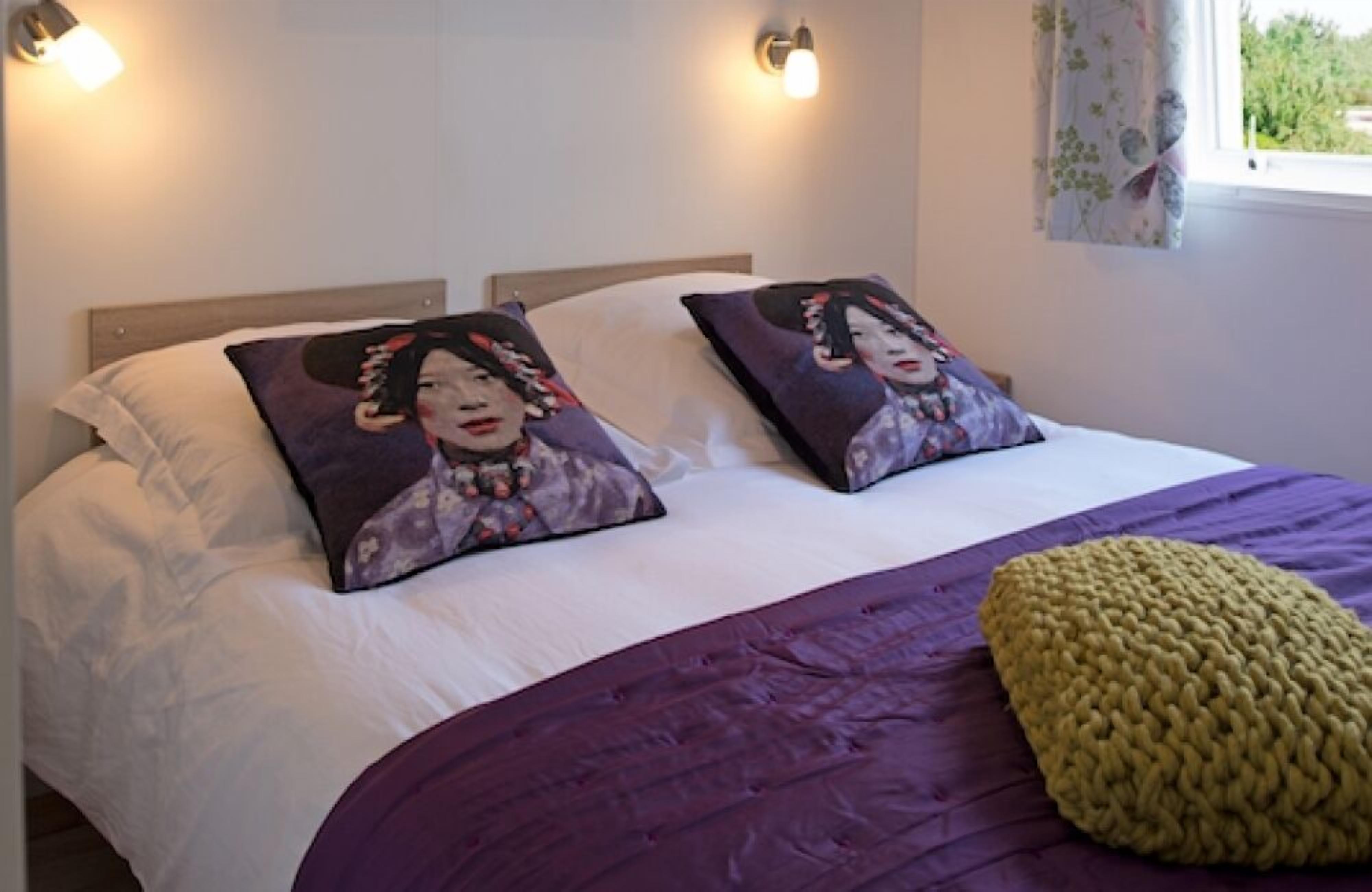 A bed with two decorative pillows, a purple blanket, and a yellow knitted throw.