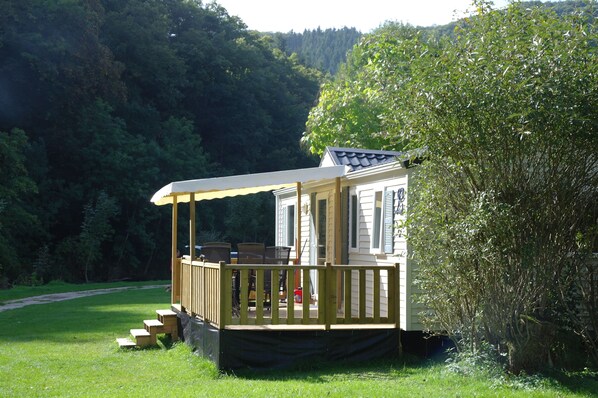 A mobile home with a porch and outdoor seating area, surrounded by a forested area.
