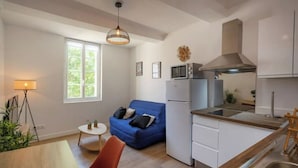 A compact living space with a kitchenette, a blue sofa, a small dining table, and a lamp. - Le Morgan - Magnificent city center apartment with parking space (Salon-de-Provence)