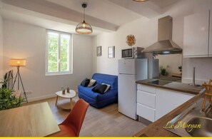 A compact living space with a kitchenette, a blue sofa, a small dining table, and a lamp.