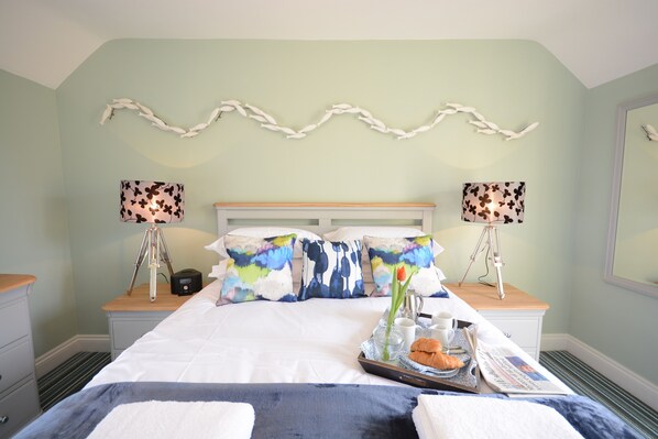A neatly made bed with a tray of breakfast items, two bedside lamps, and a decorative wall piece.