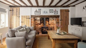 A cozy living room with a fireplace, a sofa, a coffee table, and a television. - 7 Church Street, Southwold (Reydon)