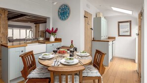 A well-lit kitchen with a round dining table, wooden chairs, and a clock on the wall. - 7 Church Street, Southwold (Reydon)