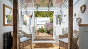 A cozy room with a glass door leading to a garden, wicker furniture, and a radiator. - 7 Church Street, Southwold (Reydon)
