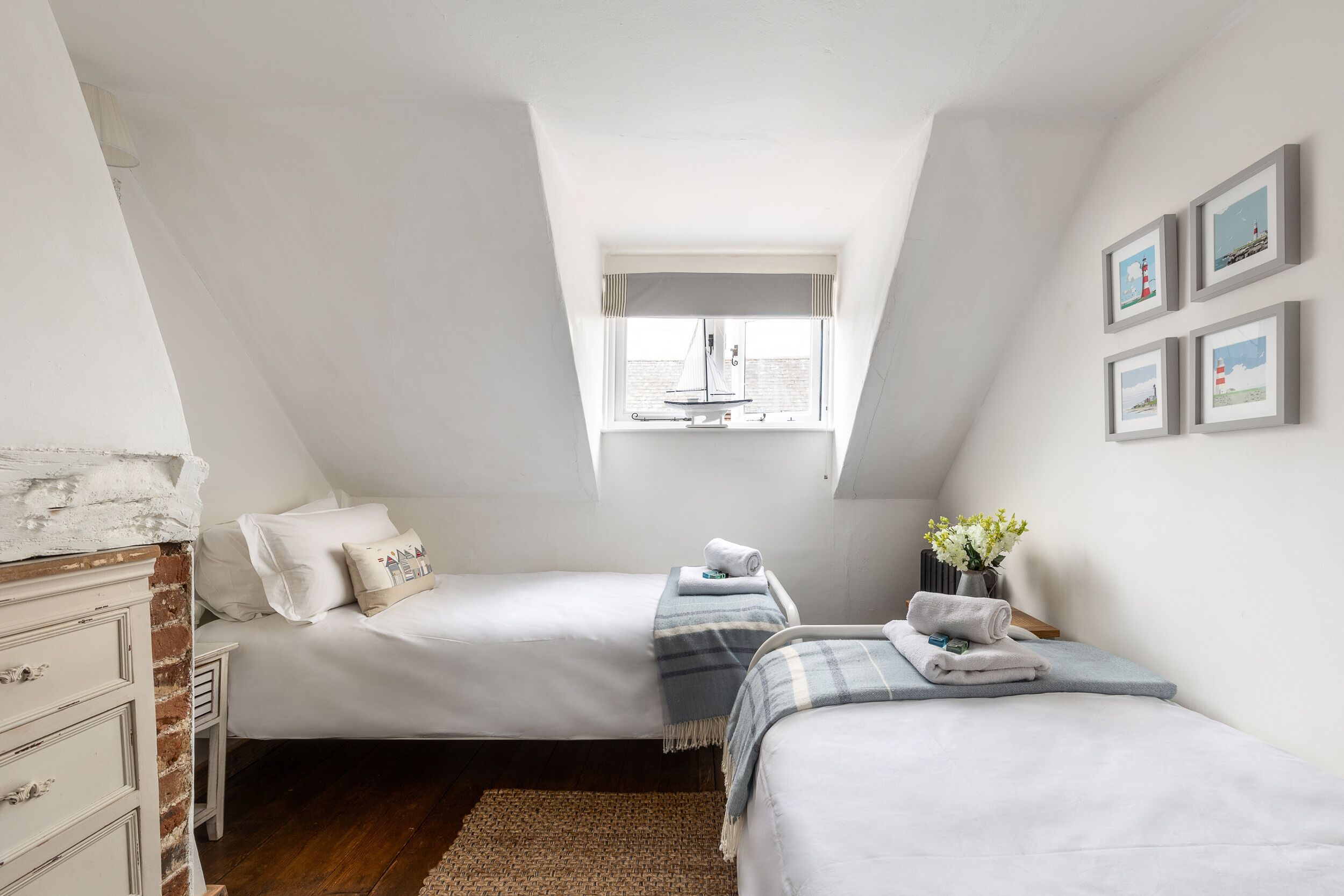 Une petite chambre bien éclairée, avec deux lits, une fenêtre donnant sur un beau paysage et une commode.