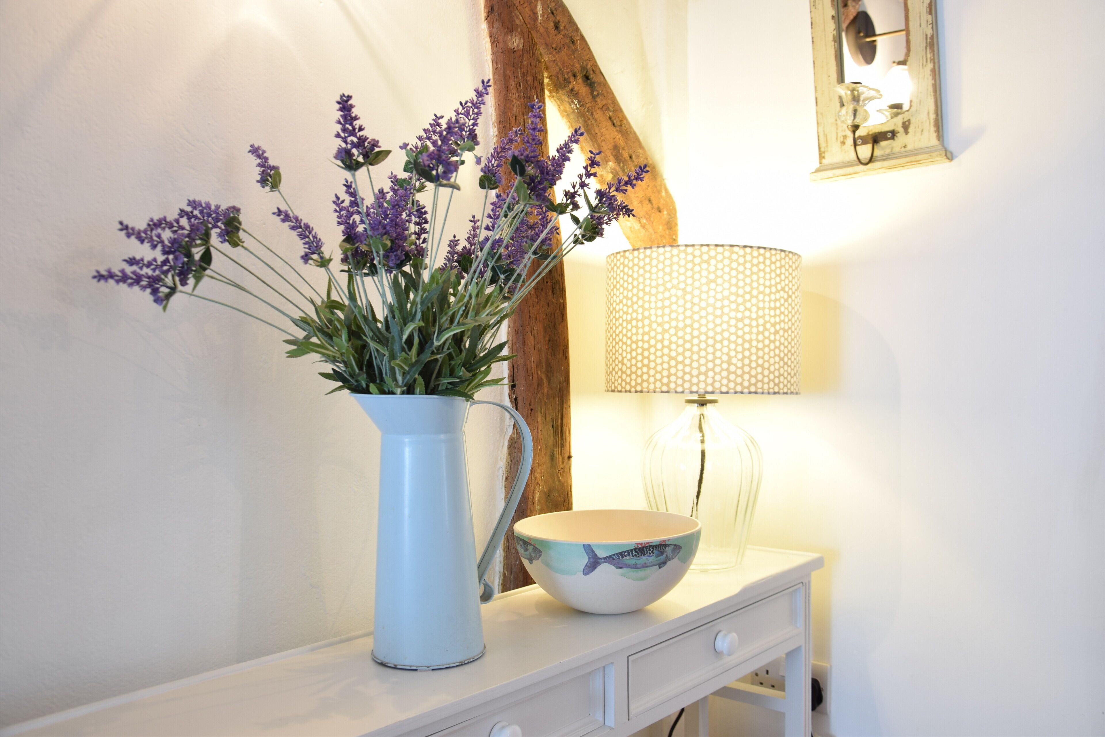 A white table with a vase of lavender flowers, a bowl, and a lamp.