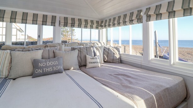 A cozy room with a large bed, striped window valances, and a view of the beach. - Valetta, Thorpeness (Leiston)
