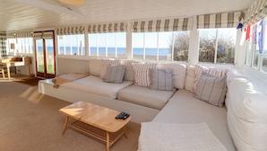 A spacious living room with a large sofa, a wooden coffee table, and a view of the sea through large windows. - Valetta, Thorpeness (Leiston)