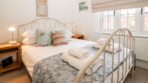 A neatly made bed with a floral duvet, a bedside lamp, and a small bedside table. - Holmleigh, Aldeburgh (Aldeburgh)