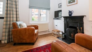 A living room with a fireplace, a television, and a window with a view of buildings outside. - Holmleigh, Aldeburgh (Aldeburgh)