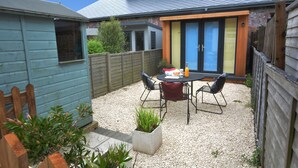 A backyard with a patio table and chairs, a wooden fence, and a blue shed. - Holmleigh, Aldeburgh (Aldeburgh)