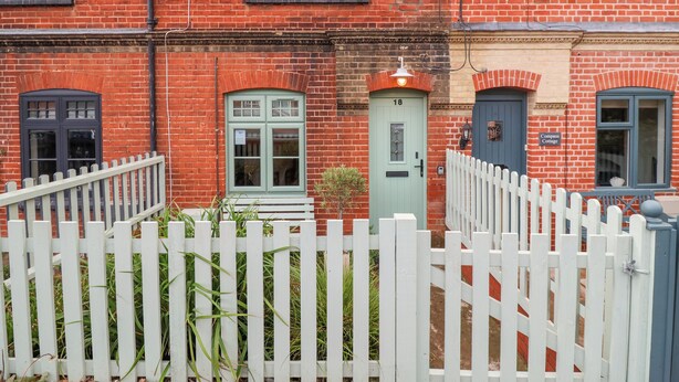 A row of red brick terraced houses with white picket fences, numbered doors, and a sign reading "Compass Cottage." - Holmleigh, Aldeburgh (Aldeburgh)