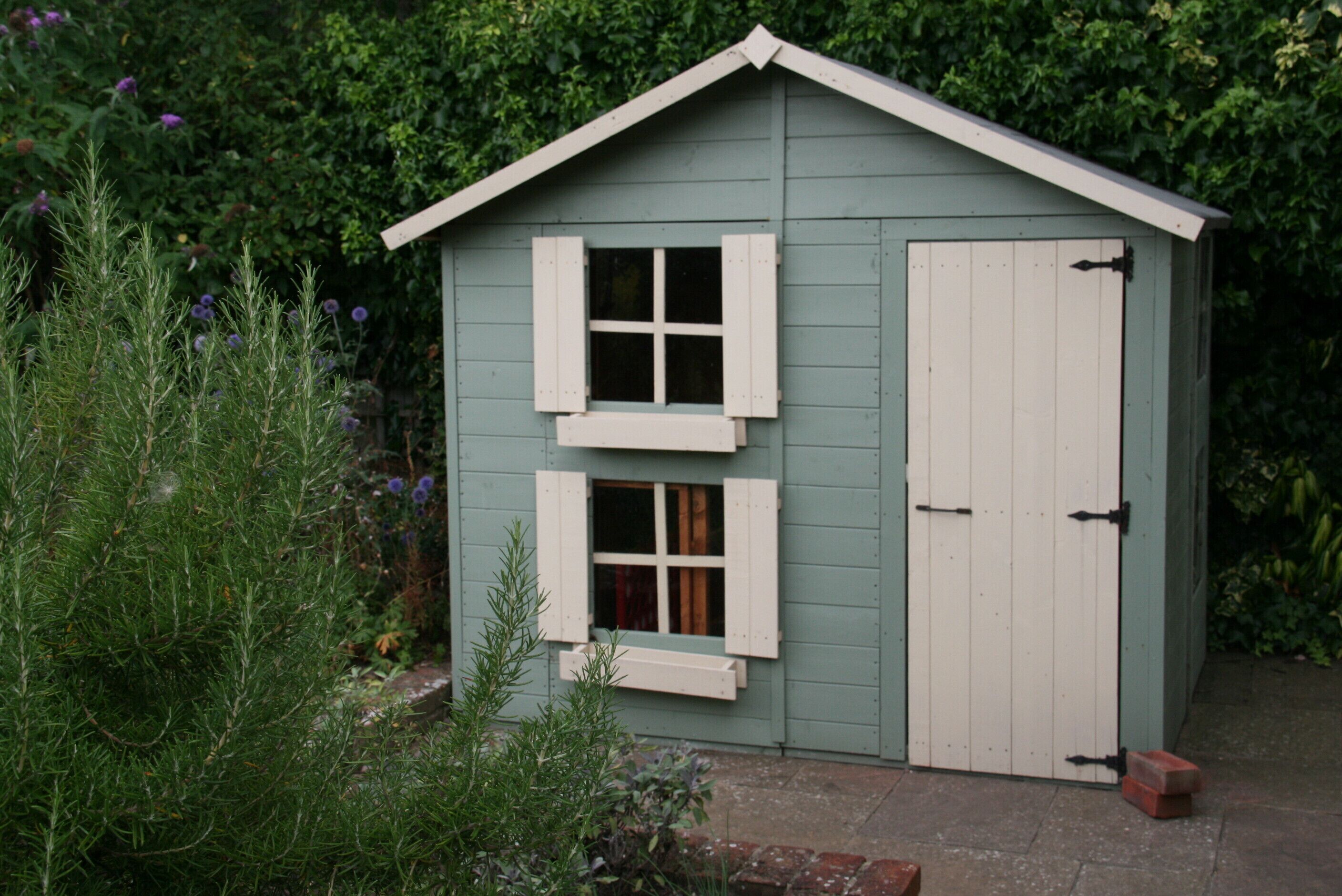 A small, single-story shed with a gabled roof and two windows with shutters.