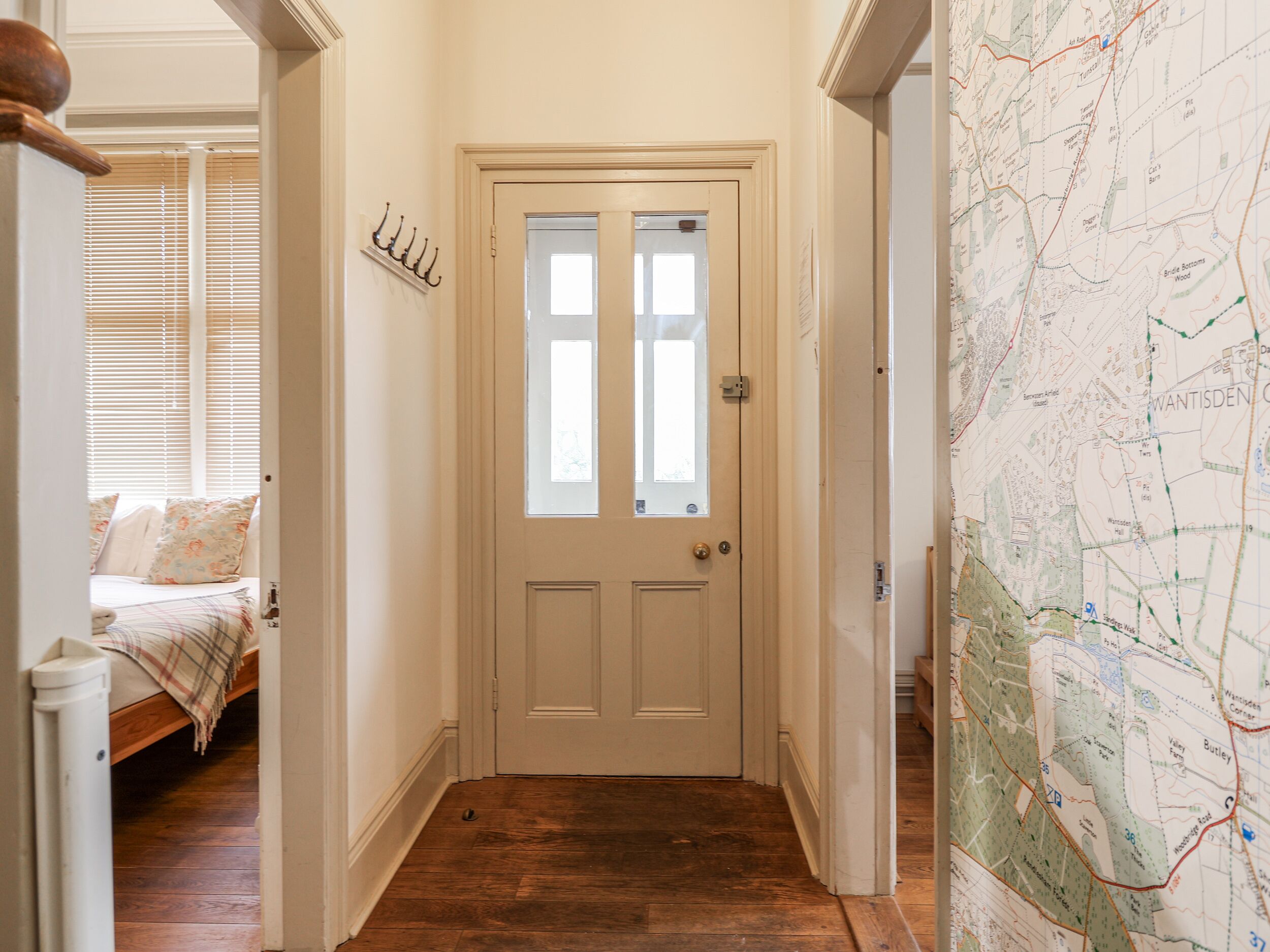 A hallway with a wooden floor, a white door with glass panels, and a map on the wall.
