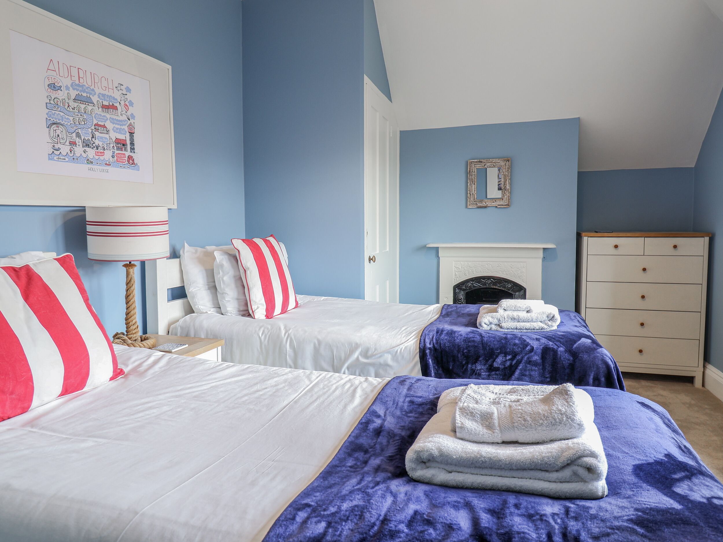 Une chambre avec deux lits, une cheminée blanche, un mur bleu et un tableau encadré accroché au mur.