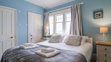 A bedroom with a bed, two bedside tables, a nightstand, a window with curtains, and a wall-mounted picture.