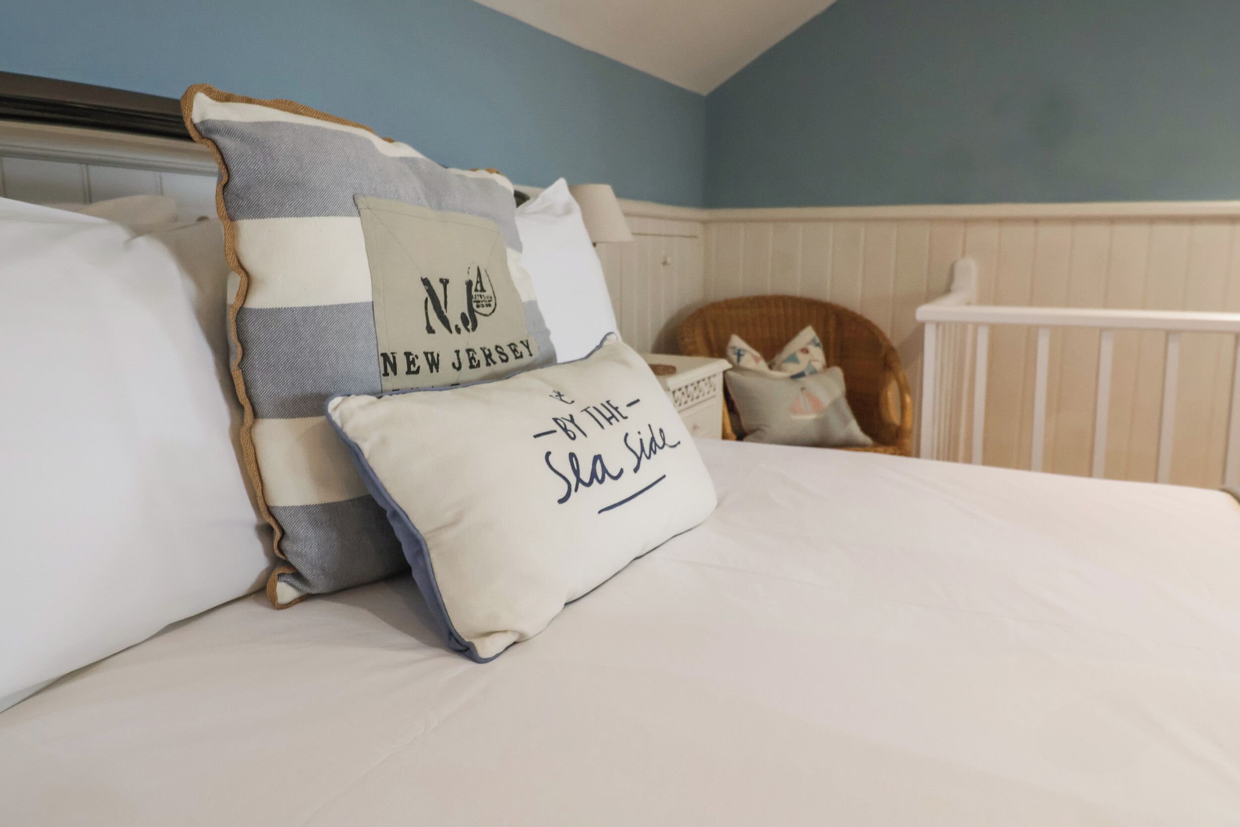 A neatly made bed with decorative pillows, a wooden headboard, and a white crib in a room with blue walls and white trim.