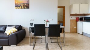 A modern living room with a black leather sofa, a dining table with two chairs, and a kitchen area with white cabinets and appliances.