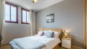 A bedroom with a bed, nightstands, a painting, and a window with curtains.