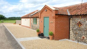 A brick building with a green door, a small porch with potted plants, and a gravel driveway.