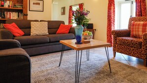 A cozy living room with a sofa, a leopard print chair, a coffee table with a vase, and a bookshelf.