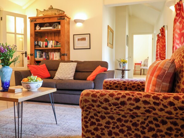 A living room with a sofa, a patterned armchair, a wooden bookshelf, and a table with a bowl of fruit. - Remus (Norwich)