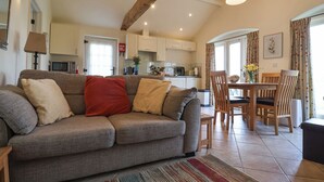 Una sala de estar acogedora con un sofá, una mesa de comedor con sillas, una zona de cocina y un amplio ventanal con cortinas.