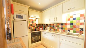 Uma cozinha compacta com armários brancos, micro-ondas, forno e uma parede de azulejos coloridos.