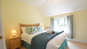 Quarto com cama, mesa de cabeceira, luminária e janela com cortinas.