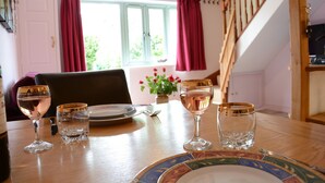 Uma mesa de jantar posta com pratos, copos e talheres, uma garrafa de vinho e um vaso com flores.