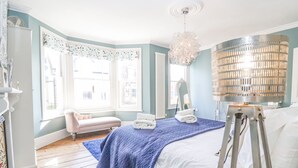 A bedroom with a bed, a bench, a standing lamp, and a radiator. - Heron House, Southwold (Reydon)
