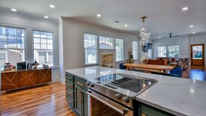 A modern kitchen with a large island, built-in oven, and a dining area with a wooden table and blue chairs.