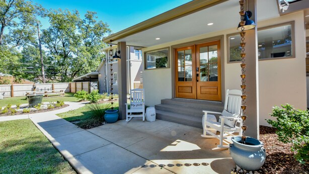 A house with a covered porch, a wooden door, and a small outdoor seating area with chairs and a table.