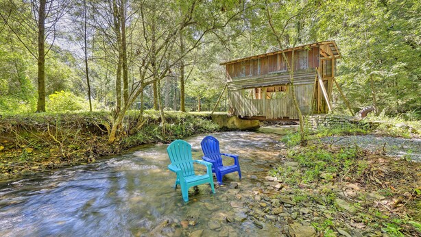 Una estructura de madera construida sobre un arroyo en un área boscosa, con dos sillas cerca del agua.