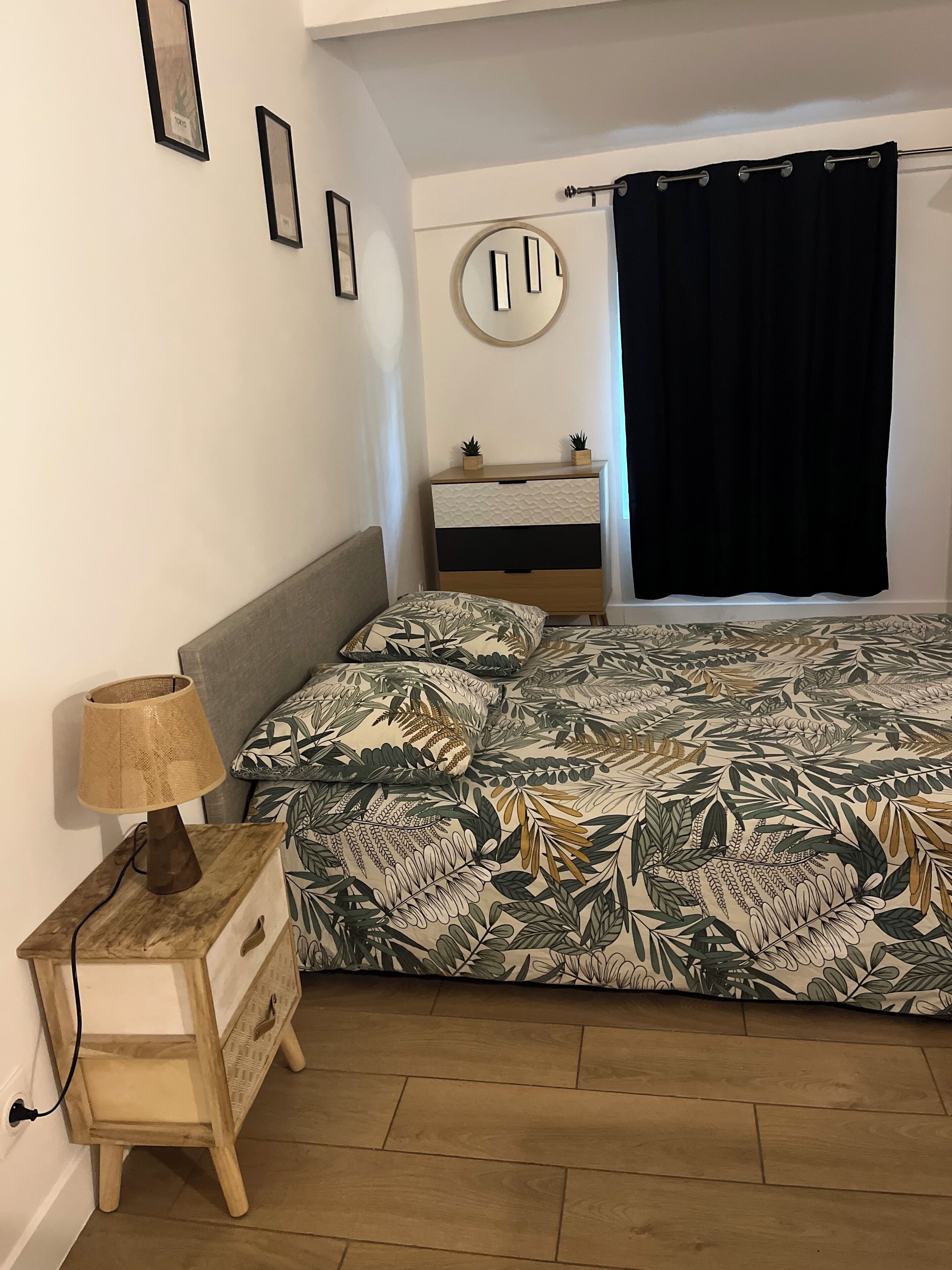 A bedroom with a bed, a nightstand, a dresser, a mirror, and a window with a curtain.
