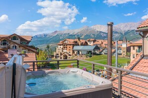 A hot tub with a mountain view, surrounded by buildings with red-tiled roofs and a mountainous landscape in the background.