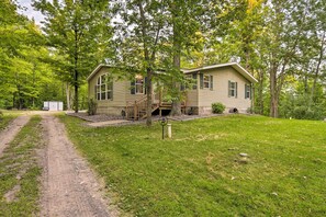 Une maison à deux étages avec un porche à l’avant, un chemin de terre menant à l’entrée et un petit abri de jardin à l’arrière.