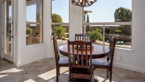 Un espace repas comprenant une table ronde et des chaises, un lustre et de grandes fenêtres donnant sur un jardin et une piscine.