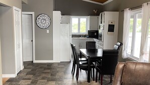 A spacious living area with a brown leather sofa, a dining table with chairs, and a kitchen in the background.