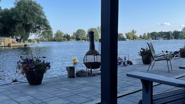 A waterfront patio with a grill, seating, and potted plants.