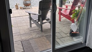 A glass door leading to a deck with a chair, a small fire pit, and a view of a lake.