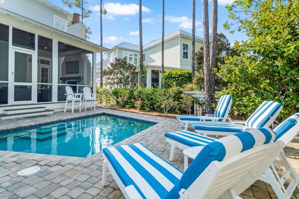 A swimming pool with lounge chairs, a covered patio, and a house with a chimney.
