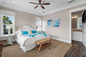 A bedroom with a bed, a ceiling fan, a window, a bedside table, and artwork on the wall.