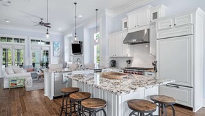 Une cuisine spacieuse avec des meubles blancs, un grand îlot central doté de tabourets et un ventilateur de plafond.
