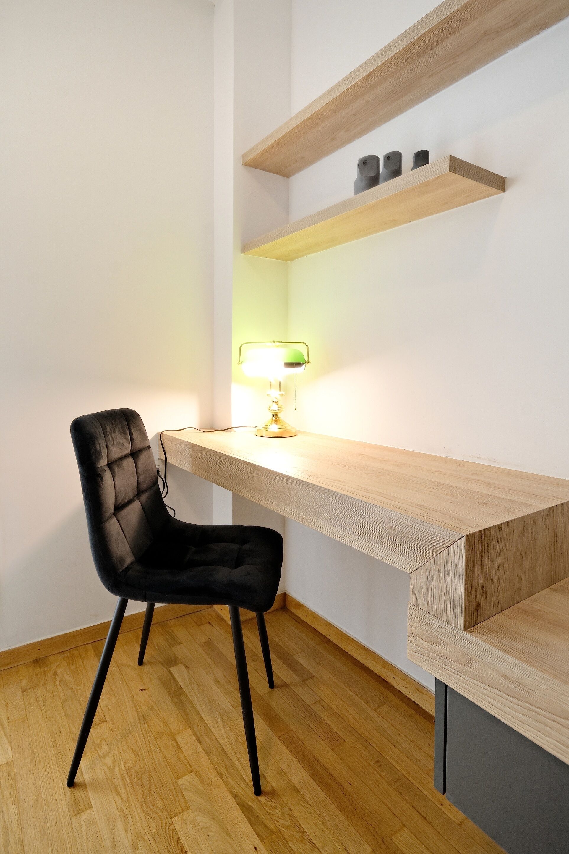 A modern workspace with a black chair, wooden desk, and shelves.