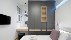 Ett modernt sovrum med en säng, en tv, en garderob och en liten hylla i trä.