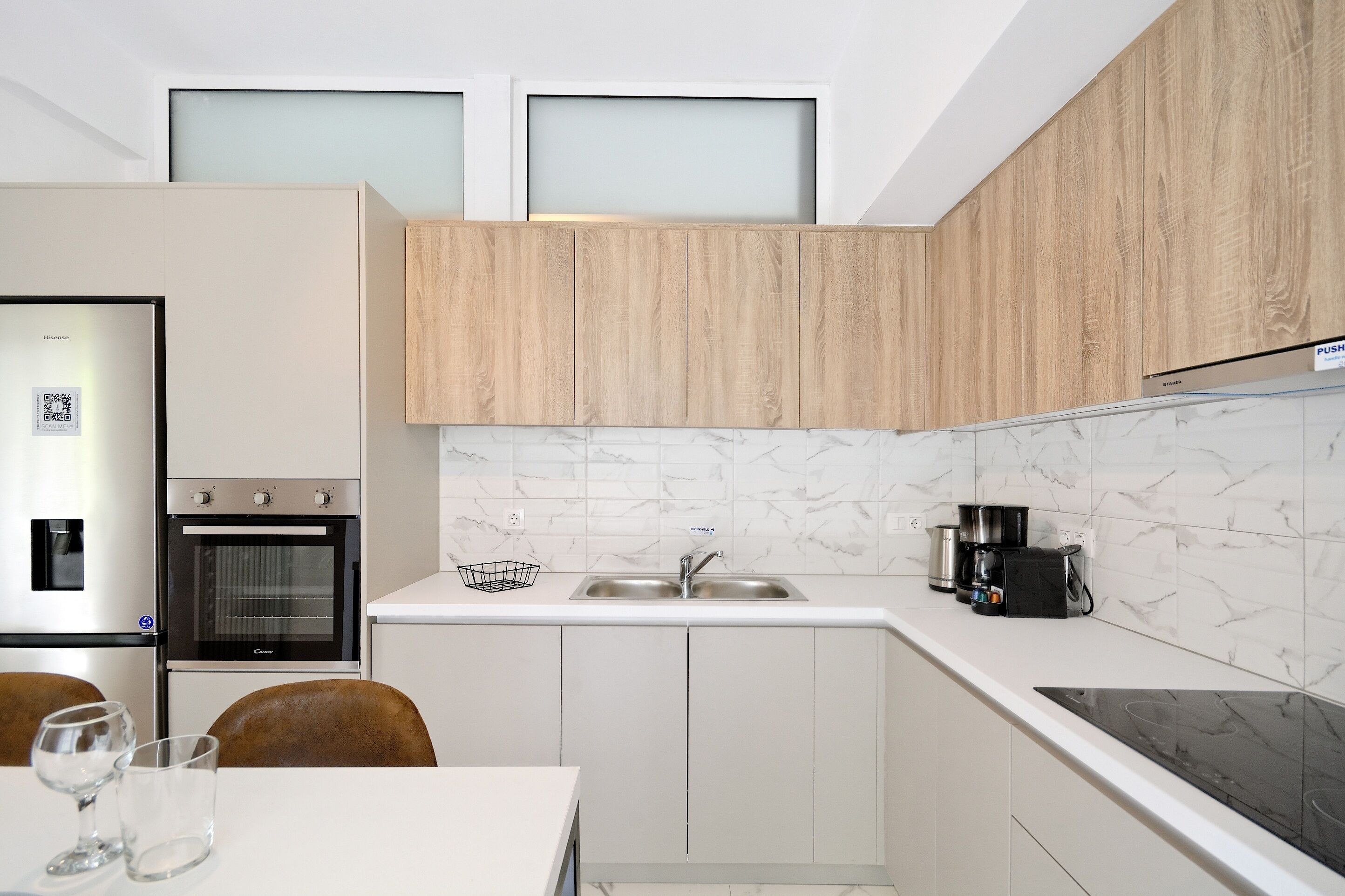 A modern kitchen with white cabinets, a built-in oven, a sink, and a countertop with a coffee maker.