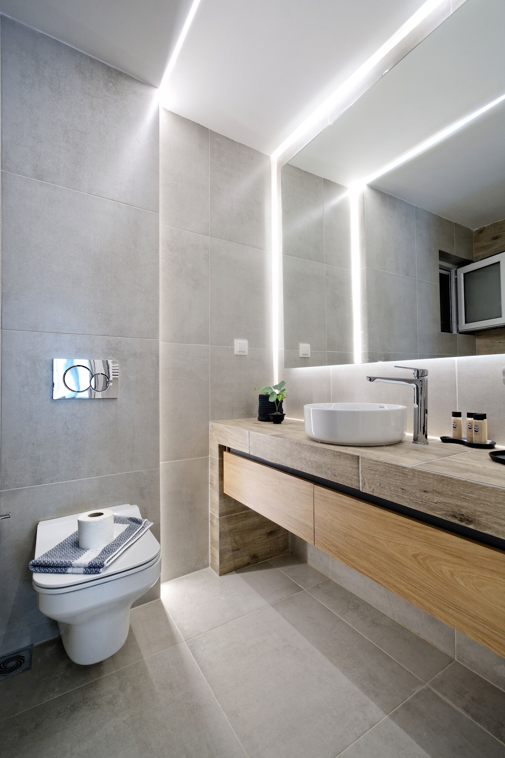 A modern bathroom with a large mirror, a white sink, and a toilet.